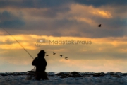 <h5>Kalamies etsii apajaa</h5><p>Auringonlaskun aikaan mies etsii uutta kala-apajaa rannalla kahlaten. Tunnus: img_7362</p>